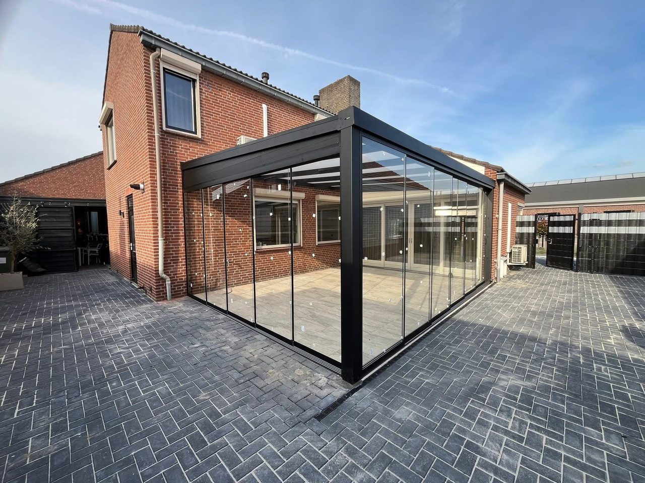 Hoekaanzicht van een antraciet tuinkamer met glazen schuifwanden aan een bakstenen woning