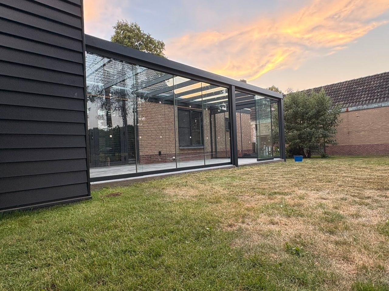 Lange tuinkamer met glazen wanden en glazen dak bij zonsondergang