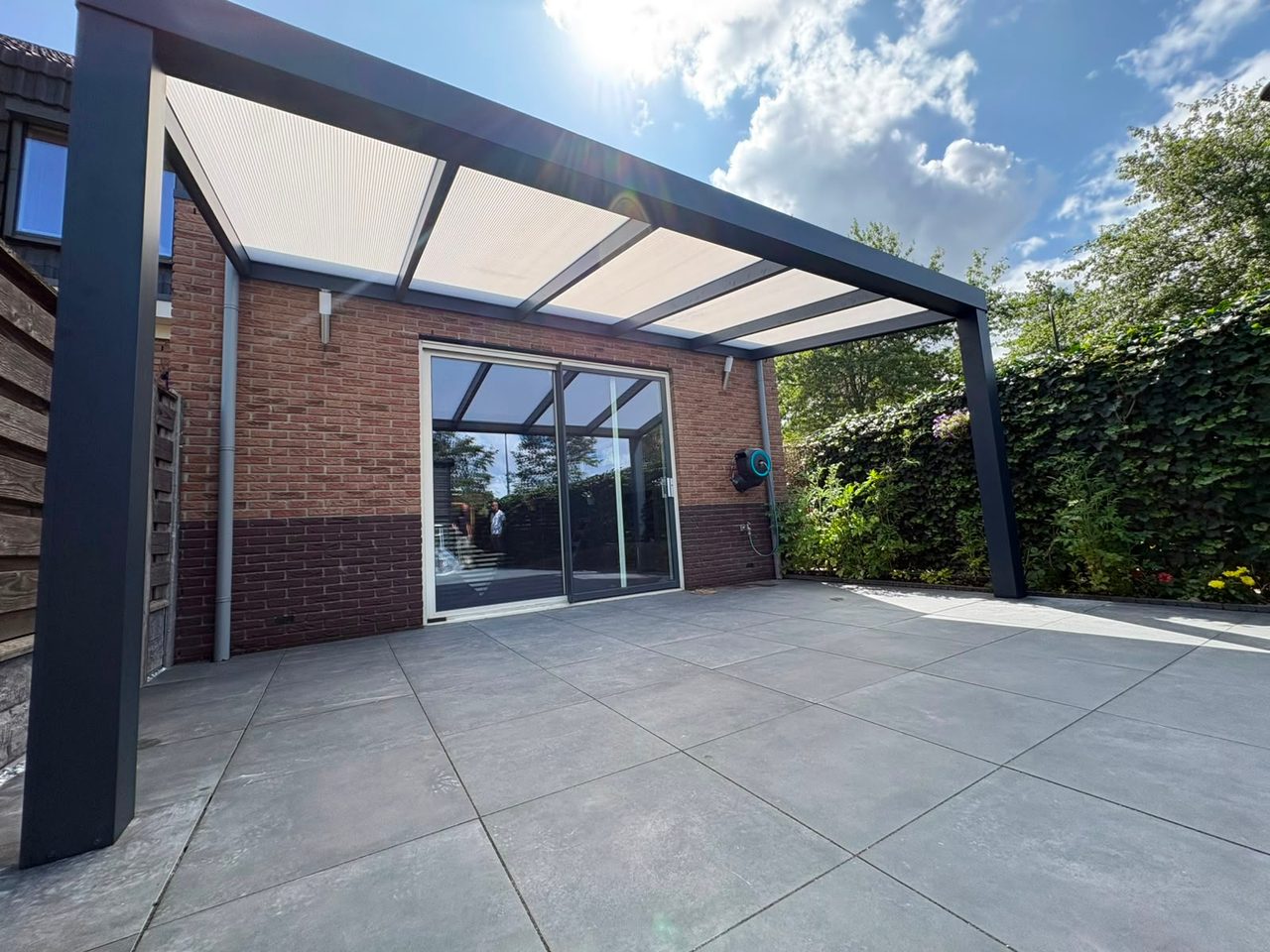 Open terrasoverkapping met opaal polycarbonaat dak boven een groot tegelterras